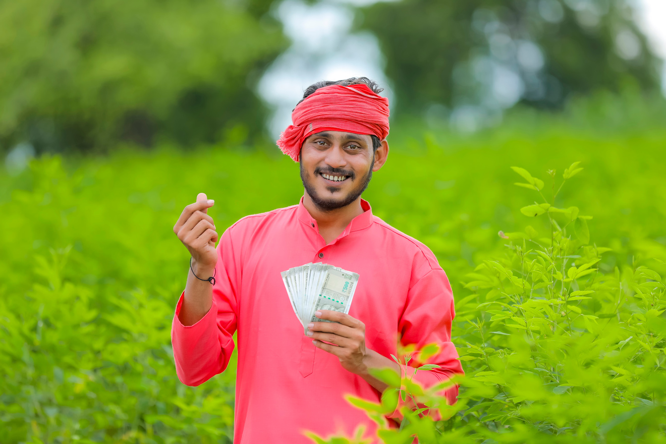 Happy young indian farmer showing indian currency in green field
